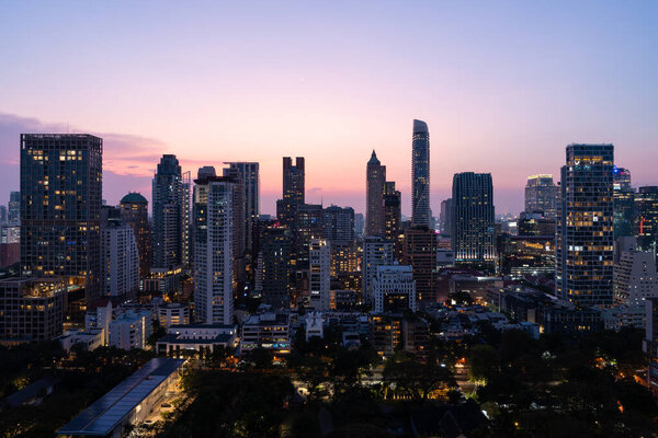 Panoramic view of Bangkok cityscape with glowing skyscrapers windows and trees in evening. Concept of tourism, business and travel in Thailand