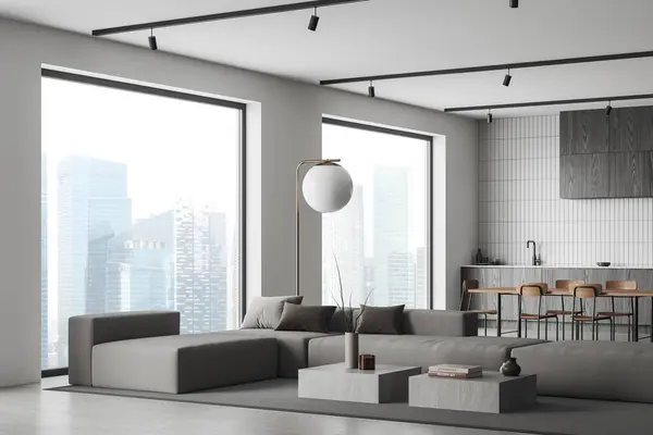 Stylish home interior with sofa and coffee table, side view dining table with chairs and cabinet, grey concrete floor. Cooking corner with cabinet and panoramic window on skyscrapers. 3D rendering