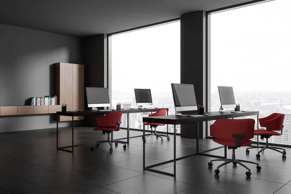 Dark office interior with armchairs and pc computers on shared desk, side view grey tile floor. Cozy coworking corner with shelf, panoramic window on Paris skyscrapers. 3D rendering