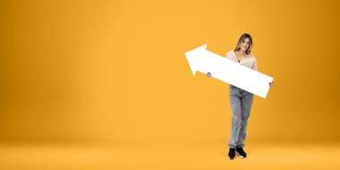 Genç, gülümseyen bir kadın. Elinde boş sarı arka planda boş bir ok tabelaları var. Yön, nokta ve tavsiye kavramı