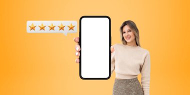 Gülümseyen genç bir kadın telefon ekranı gösteriyor, turuncu arka plan. Beş yıldız verdi, yüksek not verdi ve olumlu deneyimini paylaştı. İnceleme ve müşteri hizmetleri kavramı