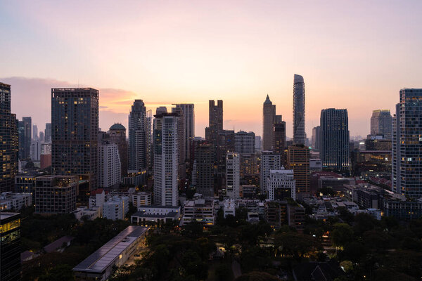 View of Bangkok city panorama with glowing skyscrapers windows and trees in evening. Concept of tourism, business and travel in Thailand