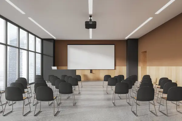 Interior of stylish lecture hall or college classroom with beige, gray and wooden walls, concrete floor, rows of gray chairs, speaker desk with computer and mock up projection screen. 3d rendering