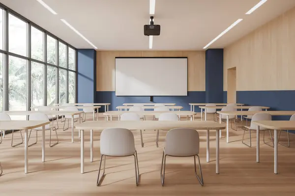 Interior of modern classroom with blue and wooden walls, wooden floor, rows of desks with white chairs and mock up projection screen. 3d rendering