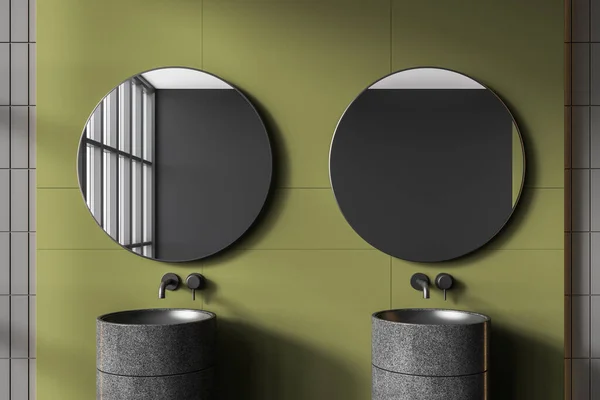 Interior of stylish bathroom with dark green and gray tiled walls and comfortable gray double sink with two round mirrors hanging above it. 3d rendering