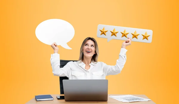 Smiling office businesswoman hands showing a mockup speech bubble, desk with laptop and signboard with five stars. Leave comment and high rating. Concept of job and companies review