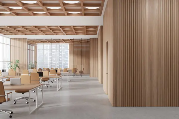 Interior of modern open space office with wooden walls, concrete floor, row of computer desks with beige chairs, glass wall meeting room in background and copy space wall on the right. 3d rendering