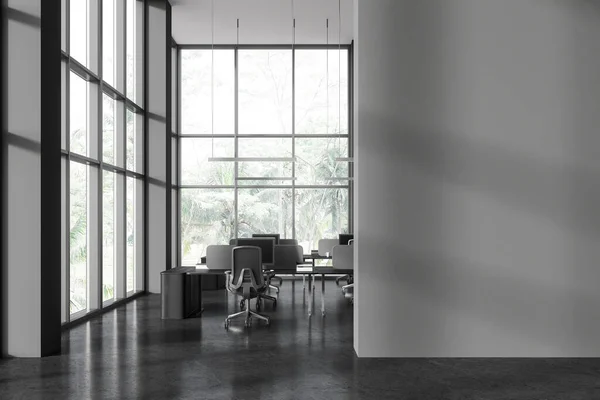 Interior of stylish open space office with gray walls, concrete floor, rows of computer desks with gray chairs and panoramic windows with tropical view. Copy space wall on the right. 3d rendering