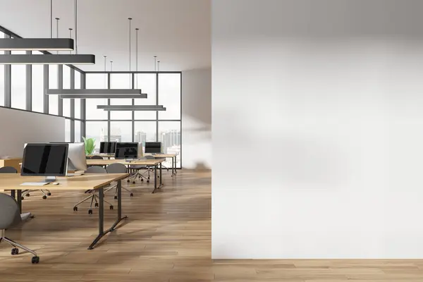 Interior of modern open space office with white walls, wooden floor, massive computer desks with gray chairs and panoramic windows with cityscape. Copy space wall on the left. 3d rendering