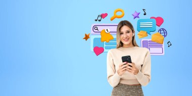 Telefon ve kulaklıkları olan mutlu genç bir kadın, fotokopi uzayının mavi arka planındaki kameraya bakıyor. Renkli çizgi film dijital dünya ikonları. Sosyal medya, iletişim ve eğlence kavramı