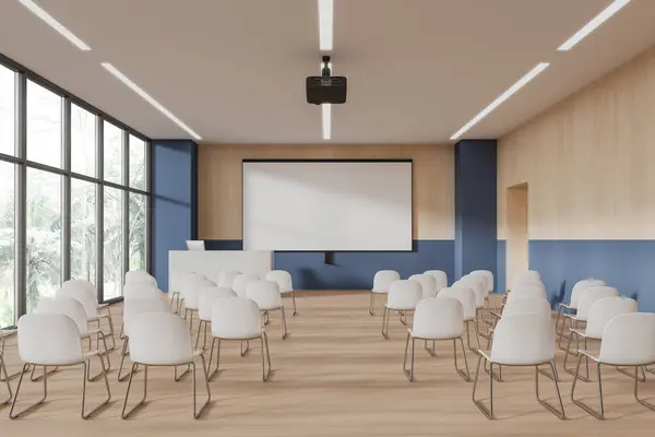 Interior of modern lecture hall or college classroom with blue and wooden walls, wooden floor, rows of white chairs, white speaker desk with computer and mock up projection screen. 3d rendering