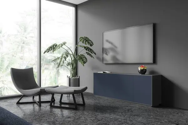 Corner of stylish living room with gray walls, concrete floor, comfortable gray armchair, dark blue dresser and modern flat screen TV set hanging above it. 3d rendering