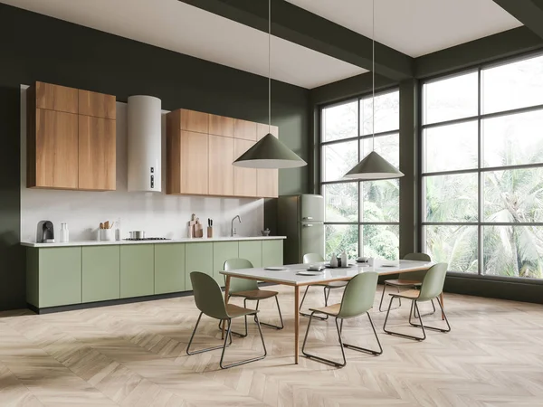 Corner of stylish kitchen with dark green walls, wooden floor, wooden cupboards, green cabinets with built in sink and cooker and long dining table with green chairs. 3d rendering