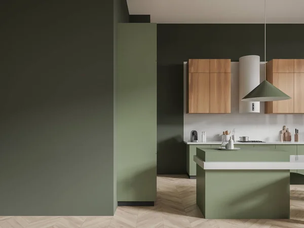 Interior of stylish kitchen with dark green walls, wooden floor, wooden cupboards, green cabinets, cozy green island and copy space wall on the left. 3d rendering