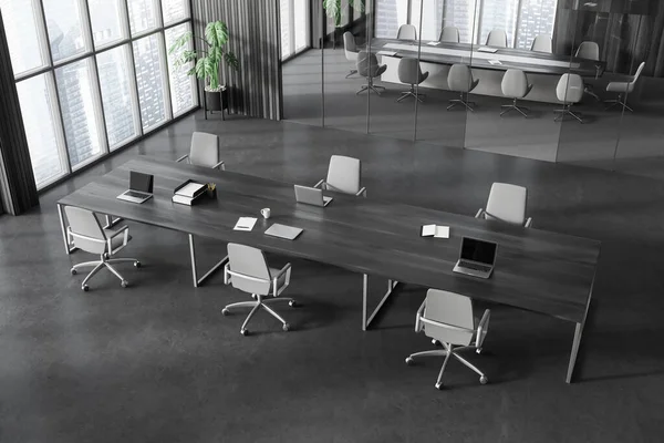 Top view of stylish open space office interior with dark wooden walls, concrete floor, wooden computer desks with laptops and gray chairs and conference room in background. 3d rendering
