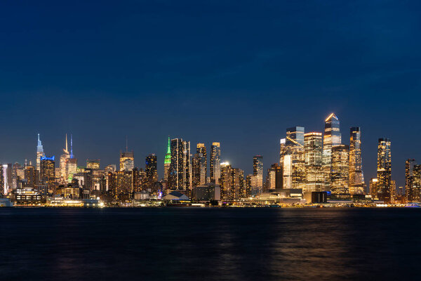 New York skyline and Hudson Yards at night, panoramic view on office buildings with lights, corporate financial center and waterfront. Manhattan west side and river