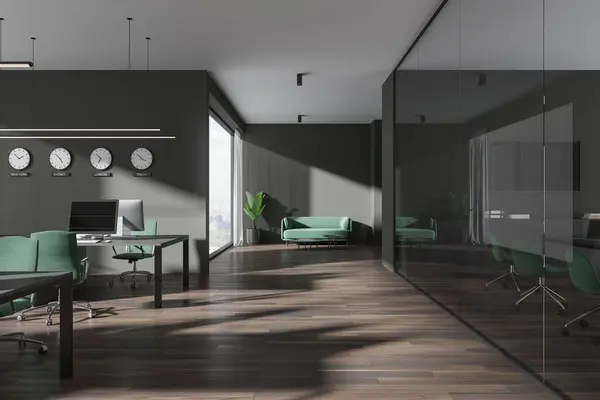 Interior of stylish open space office with dark gray walls, brown floor, row of computer tables with green chairs, cozy green sofa and clocks showing world time. 3d rendering