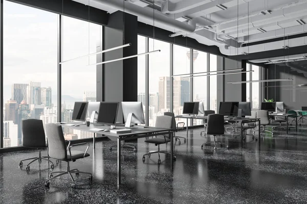 Dark office interior with coworking area, pc computers on shared desk in row, side view grey granite floor. Glass meeting room and panoramic window on Kuala Lumpur skyscrapers. 3D rendering