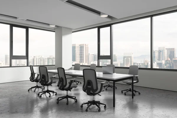 White office interior with chairs and meeting board, side view furniture with laptop on grey concrete floor. Negotiation space and panoramic window on Kuala Lumpur skyscrapers. 3D rendering