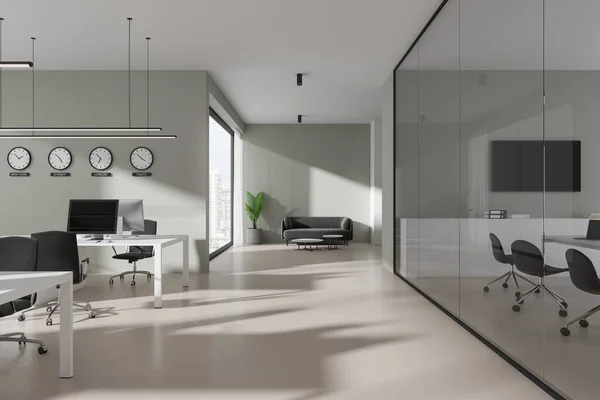 Interior of modern open space office with light gray walls, concrete floor, row of computer tables with black chairs, cozy gray sofa and clocks showing world time. 3d rendering