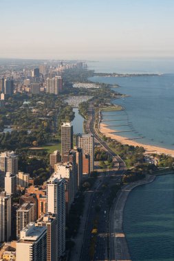 Ofis binaları ve Michigan Gölü ile Chicago ufuk çizgisi, yeşil parklı kıyı şeridi. İş dünyasının panoramik manzarası. Dikey hava aracı görüntüleri. Illinois, ABD, Kuzey Amerika