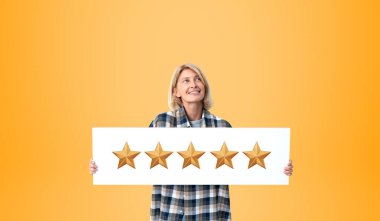 Neşeli genç Avrupalı kadın portresi günlük kıyafetler giymiş ve turuncu arka planda duran beş yıldızlı bir tabela taşıyor. Ürün ve hizmet değerlendirmesi kavramı