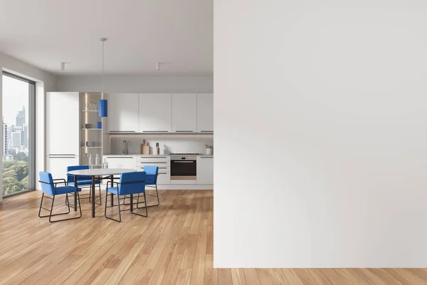 Interior of modern kitchen with white walls, wooden floor, cozy white cupboards and cabinets, round dining table with blue chairs and copy space wall on the right. 3d rendering