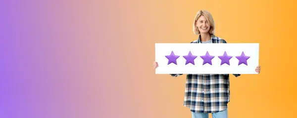 Portrait of happy young woman in casual clothes holding five star sign standing over purple copy space background. Concept of product and service evaluation and client feedback