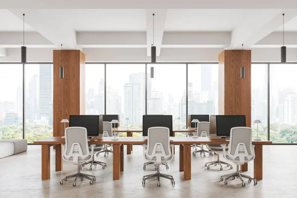 White workplace interior with armchairs and pc computers in row, light concrete floor. Stylish coworking loft with panoramic window on New York skyscrapers. 3D rendering