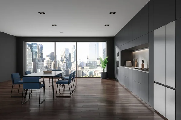 Dark home kitchen interior with dinner table and blue chairs, side view. Cooking cabinet with sink, oven and refrigerator on hardwood floor. Panoramic window on New York skyscrapers. 3D rendering