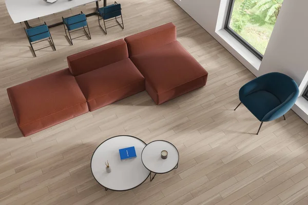 Top view of modern living room with white walls, wooden floor, comfortable brown couch standing near round coffee tables and dining room with long table and chairs next to it. 3d rendering