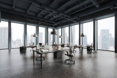 Gri duvarları, beton zemini, dizüstü bilgisayarları ve panoramik pencereleri olan gri bilgisayar masaları olan şık bir açık uzay ofisinin köşesi.