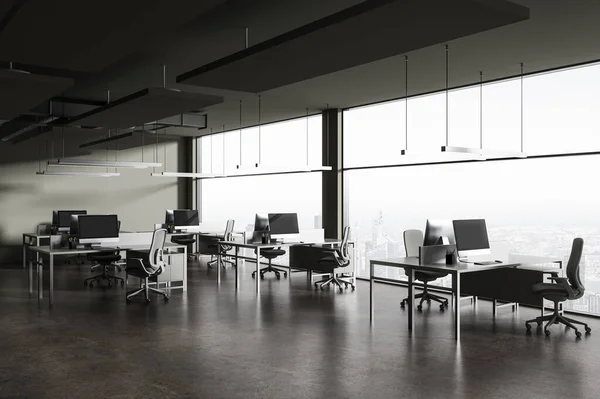 Dark coworking interior with pc computers on work table in row, side view grey concrete floor. Minimalist work corner with panoramic window on Paris skyscrapers. 3D rendering
