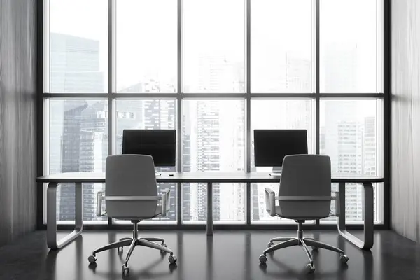 Dark office loft interior with two pc desktop, coworking area with armchairs and shared desk on grey concrete floor. Panoramic window on Singapore skyscrapers. 3D rendering