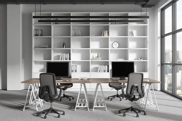 White office interior with pc computers on shared table, shelf with art decoration on carpet. Scandinavian workplace with panoramic window on Kuala Lumpur skyscrapers. 3D rendering
