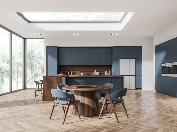 Interior of modern kitchen with white walls, wooden floor, blue cabinets and cupboards, island with stools and round table with blue chairs. 3d rendering