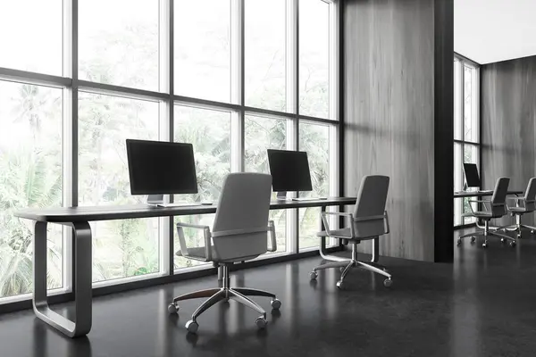 Corner of stylish open space office with dark wooden walls, concrete floor and long computer tables with gray chairs standing near big windows. 3d rendering