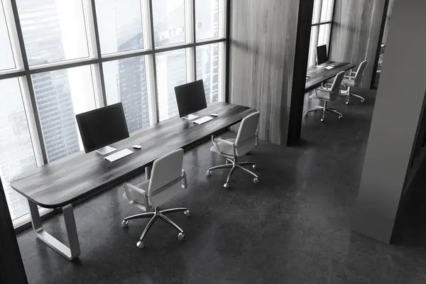 Top view of dark office loft interior with pc computers in row, coworking corner with armchairs and shared desk on grey concrete floor. Panoramic window on Singapore skyscrapers. 3D rendering