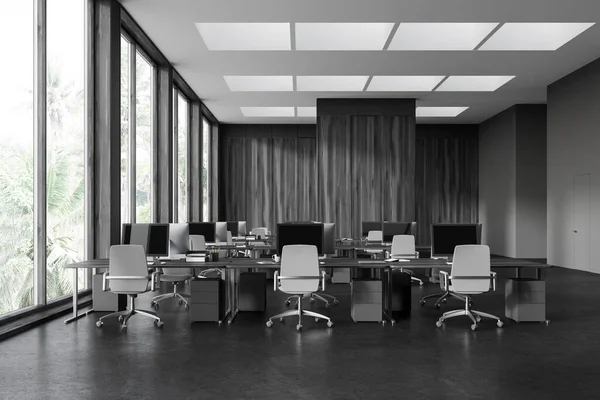 Black wooden office interior with pc computers and desk in row, grey concrete floor. Stylish coworking space with panoramic window on tropics. 3D rendering