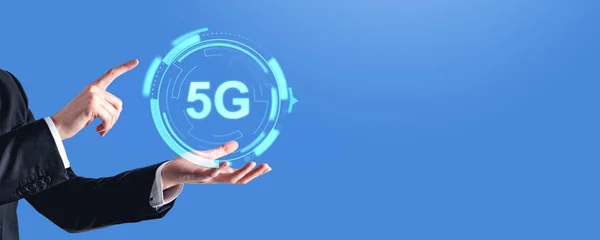 Businessman hand and finger touching 5G icon, wide format on copy space empty blue background. Glowing hologram of internet connection and digital technology