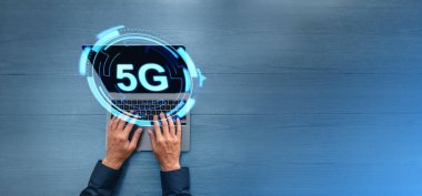 İnsan elinin dizüstü bilgisayarda yazışının üst görüntüsü, geniş formatta parlayan 5G simgesi, kopyalama masası. İnternet bağlantısı ve modern internet teknolojisinin parlayan hologramı