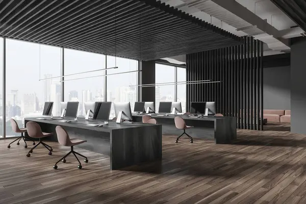 Dark office interior with coworking room and pc computers, side view workspace with table and armchairs in row on hardwood floor. Panoramic window on Singapore skyscrapers. 3D rendering