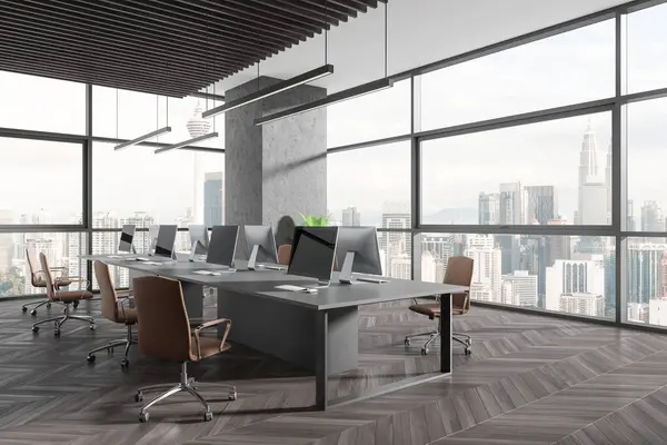 Dark office interior with pc desktop on table in row, side view hardwood floor. Stylish workspace with panoramic window on Kuala Lumpur skyscrapers. 3D rendering