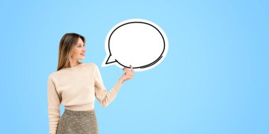 Happy beautiful woman showing a mock up blank thought bubble, copy space cloud on light blue background. Concept of recommendation, opinion, choice and offer