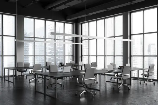 Dark office interior with laptop on table and chairs in row, side view grey concrete floor. Stylish office work corner with panoramic window on Singapore skyscrapers. 3D rendering