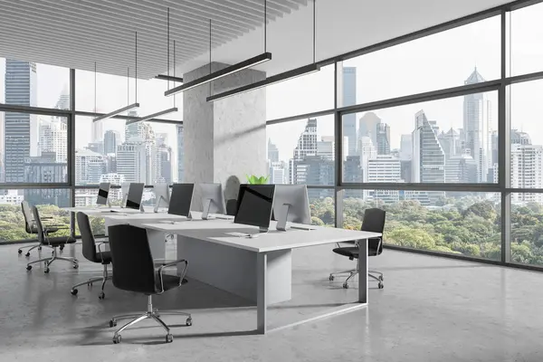 Industrial office interior with pc computers and shared desk in row, side view grey concrete floor. Stylish coworking corner with panoramic window on Bangkok skyscrapers. 3D rendering