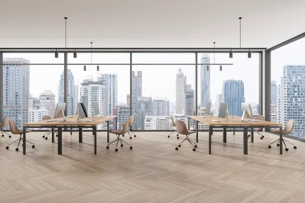 Minimalist office interior with pc monitors on shared desk in row, hardwood floor. Stylish coworking space with panoramic window on Bangkok skyscrapers. 3D rendering