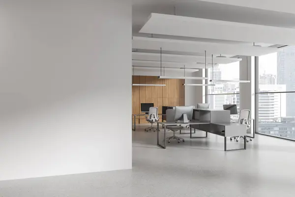 Corner of modern open space office with white walls, concrete floor, rows of computer desks with gray chairs and copy space wall on the left. 3d rendering