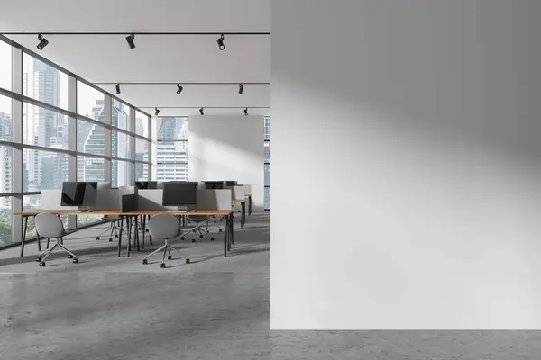 Interior of modern open space office with white walls, carpeted floor and rows of computer desks with gray chairs standing near panoramic window with cityscape. Copy space wall. 3d rendering