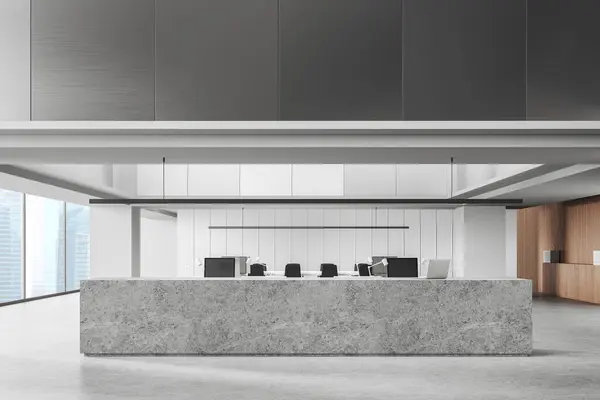 Interior of modern office hall with white and gray walls, concrete floor and long gray reception counter with laptop standing on it. 3d rendering